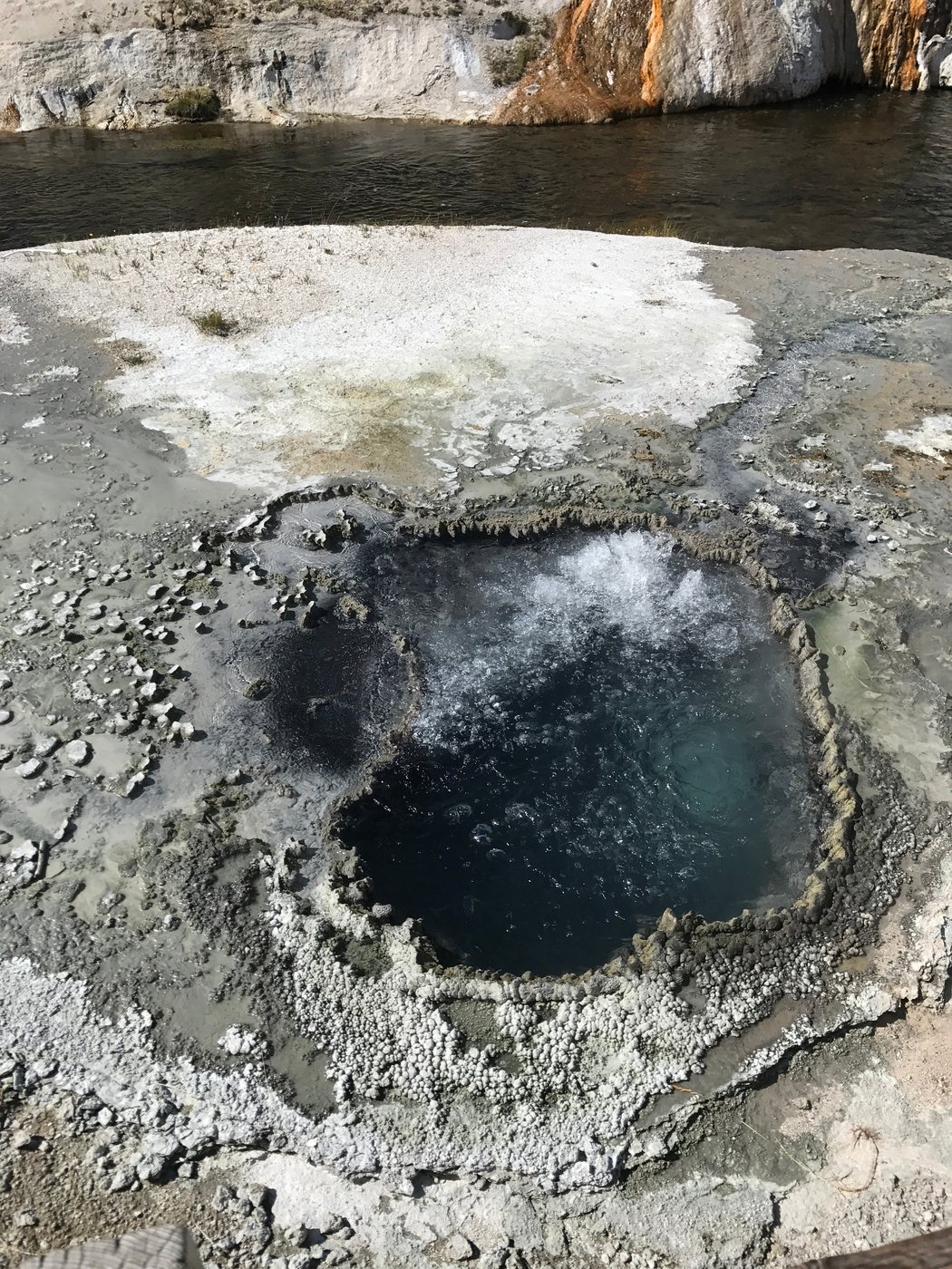 Dark bubbling geothermal pool surrounded by mineral deposits