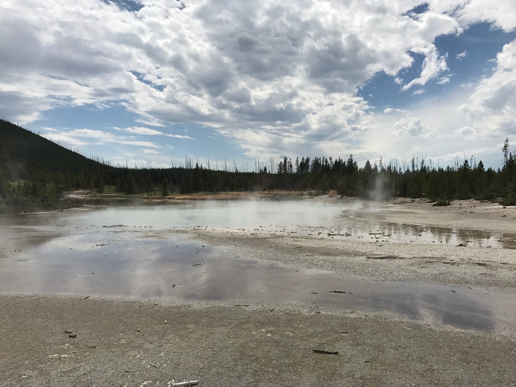 Steaming geothermal basin beneath a large dramatic sky